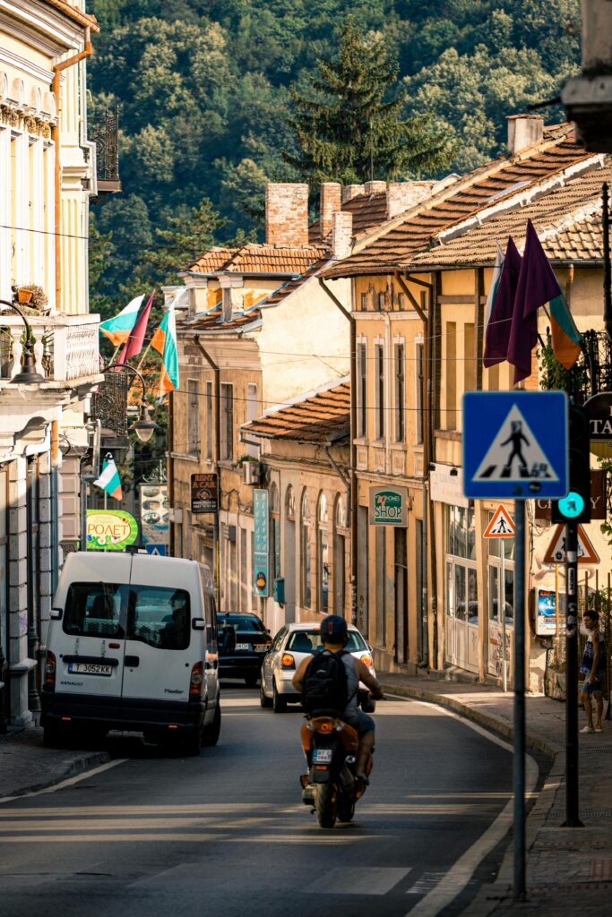 הטיולים שלנו Motorcyclist rides through the bustling streets of Veliko Tarnovo, showcasing vibrant urban life.
