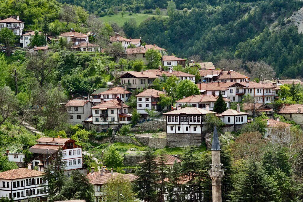 הטיולים שלנו Picturesque Ottoman village nestled in lush green hills, showcasing traditional architecture with red roofs.